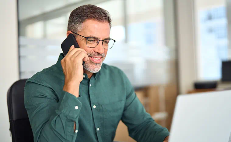 Businessman making call on cellphone using laptop in office. Smiling busy mature old professional business man manager talking on phone working at laptop computer communicating at work.