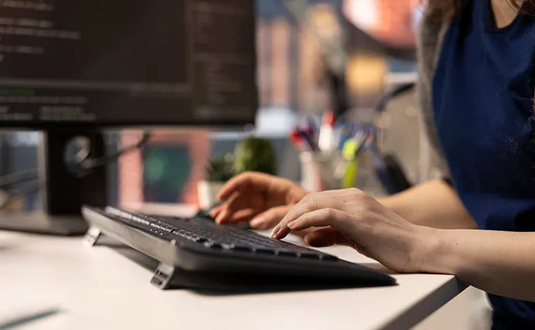 Administrator at office typing in information into a database. Close up.