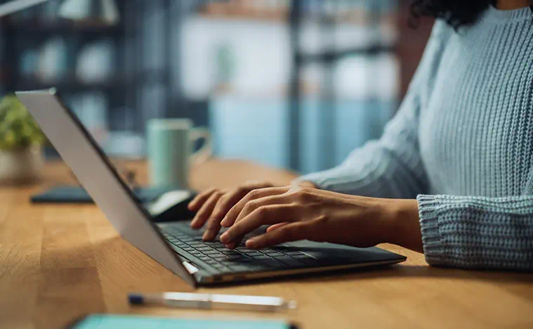Close up of a woman typing on her computer in a coffee shop.